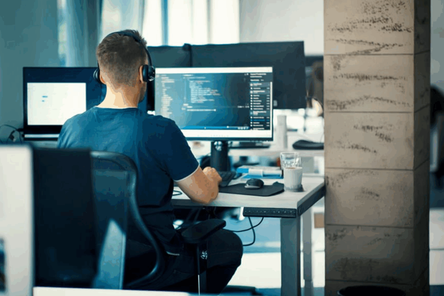 Young man sitting at a computer writing code while wearing headphones