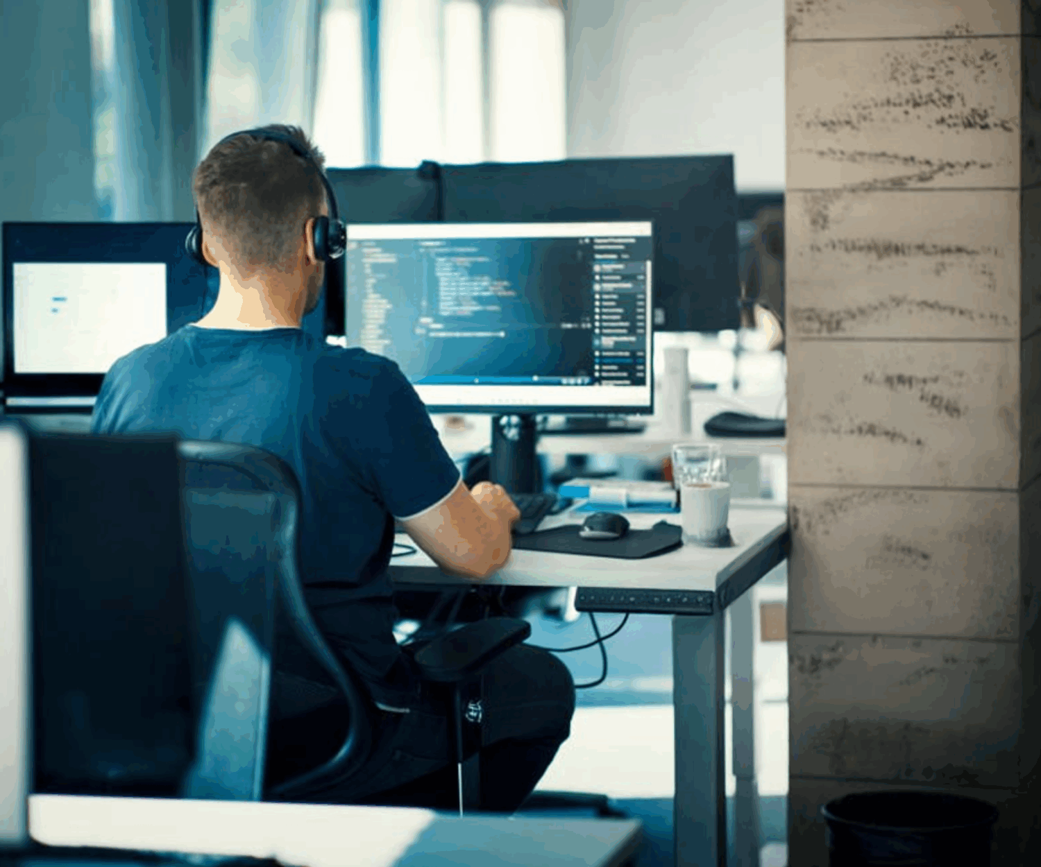 Young man sitting at a computer writing code while wearing headphones