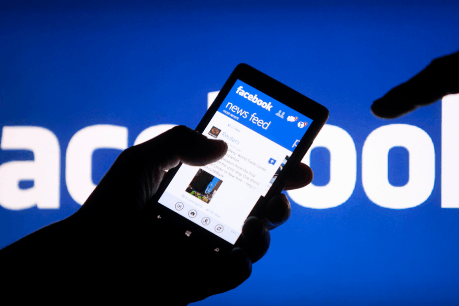 Person holding a phone in their hand showing a Facebook newsfeed