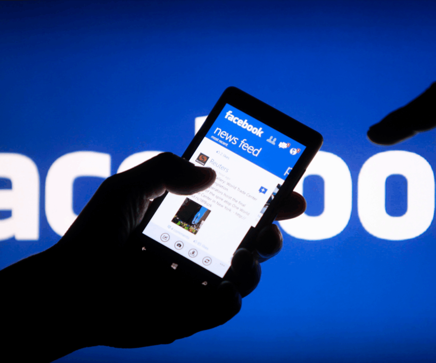 Person holding a phone in their hand showing a Facebook newsfeed