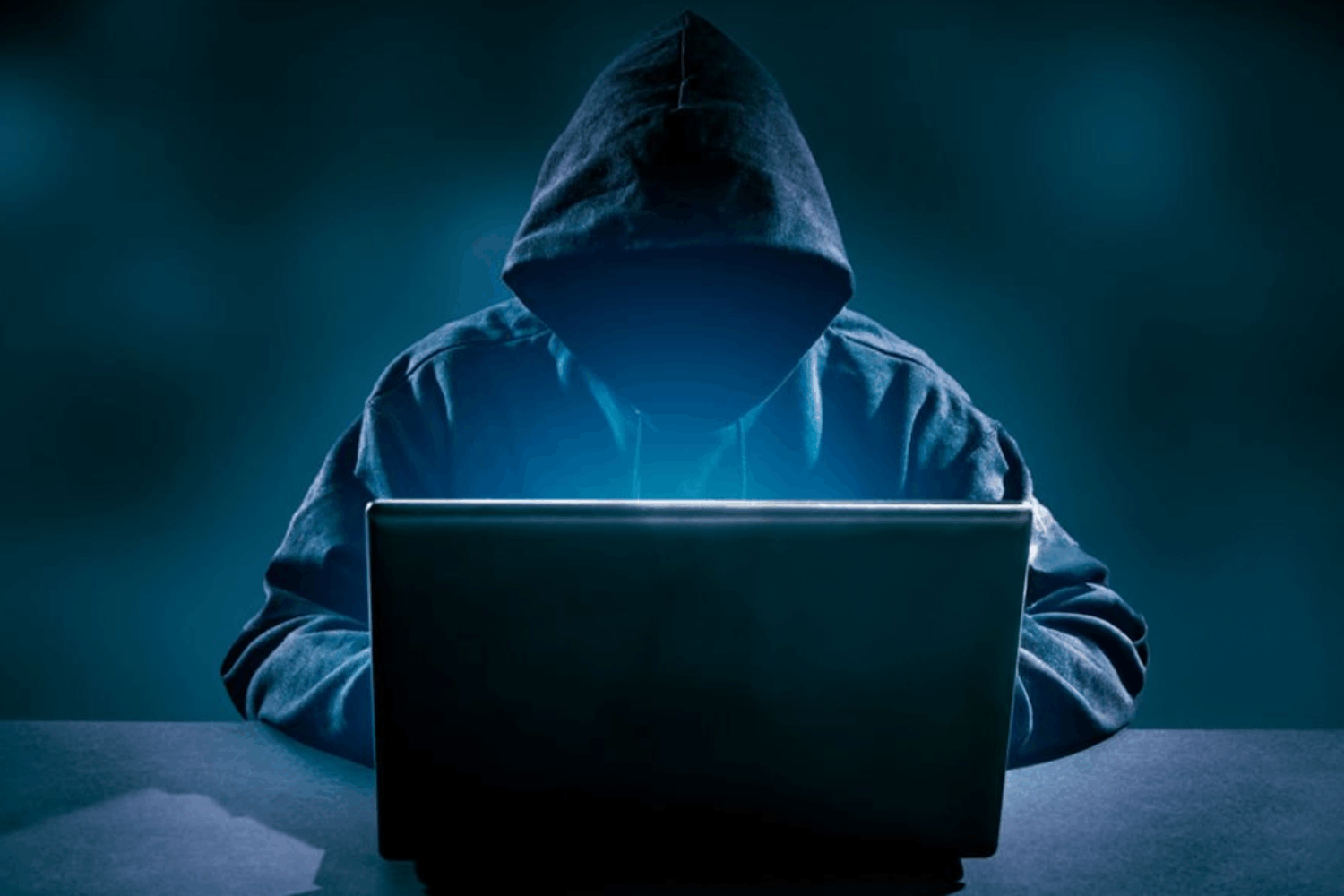 Hacker at a laptop wearing a hoodie in a dark room
