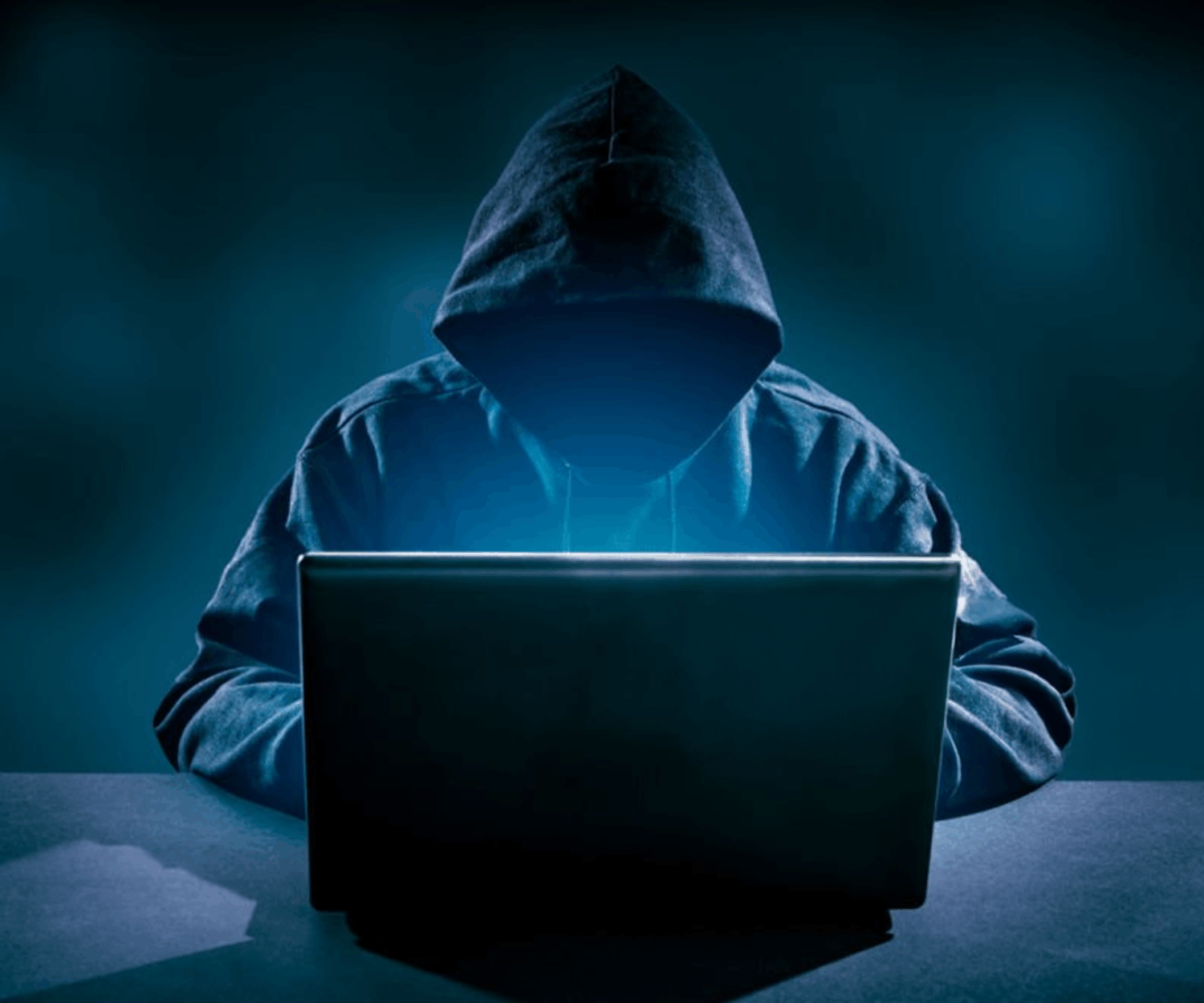 Hacker at a laptop wearing a hoodie in a dark room